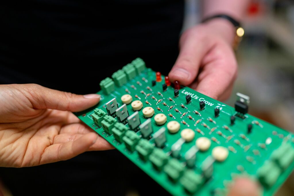 Close-up of hands holding a green circuit board used for electronic projects.